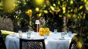 Mesa al aire libre con mantel blanco, copas de vidrio verde y una piña como centro de mesa.