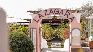 Un arco de entrada con 'LA ZAGARA' escrito, que da paso a un sendero con plantas en macetas y un reloj.