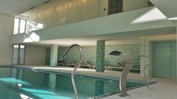 Una piscina interior moderna con agua cristalina, sillones de descanso y techo de vidrio.