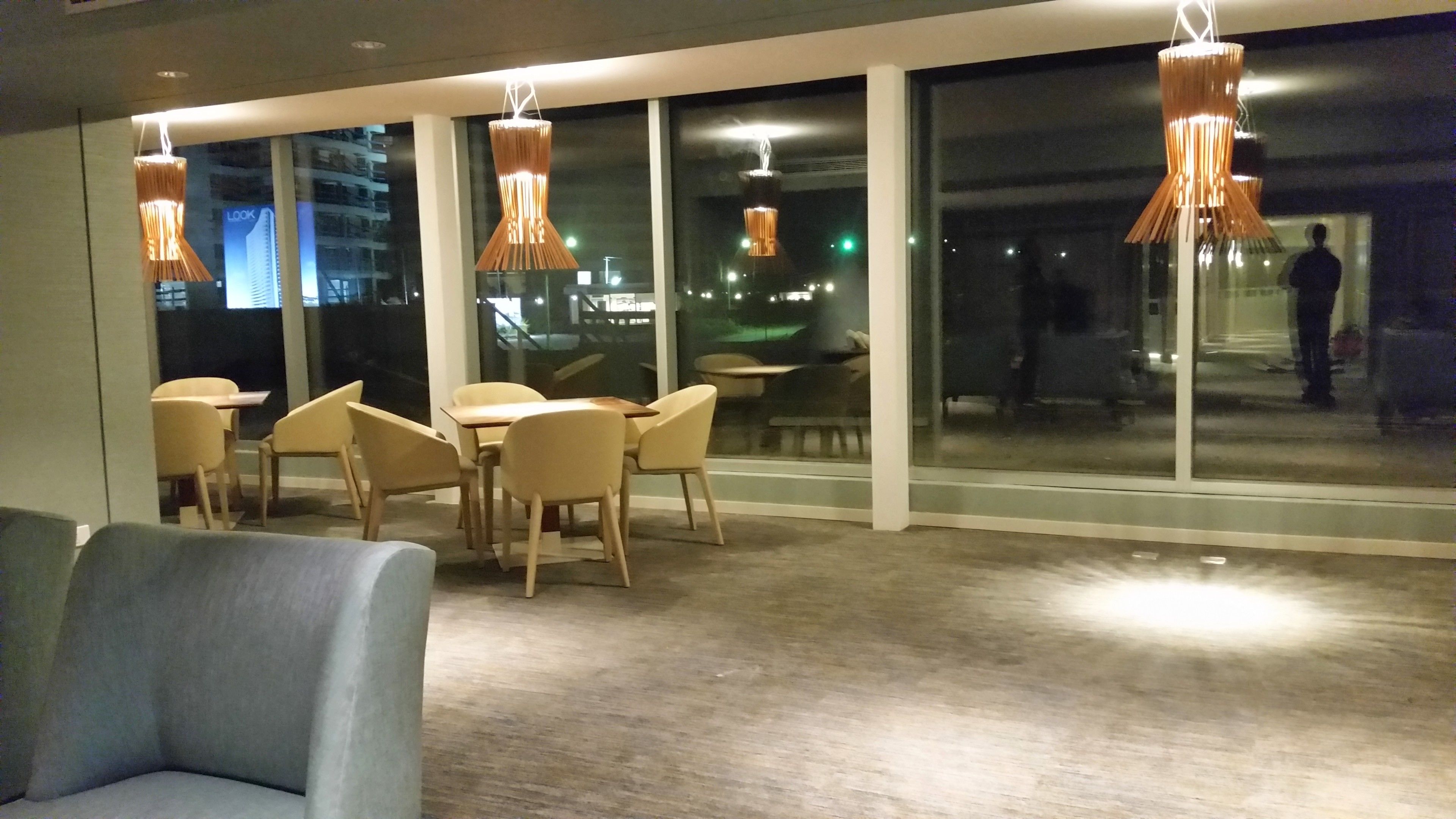 Een modern interieur met een eetgedeelte met ronde tafels en stoelen, grote ramen met uitzicht op de stad en hangende吊灯.