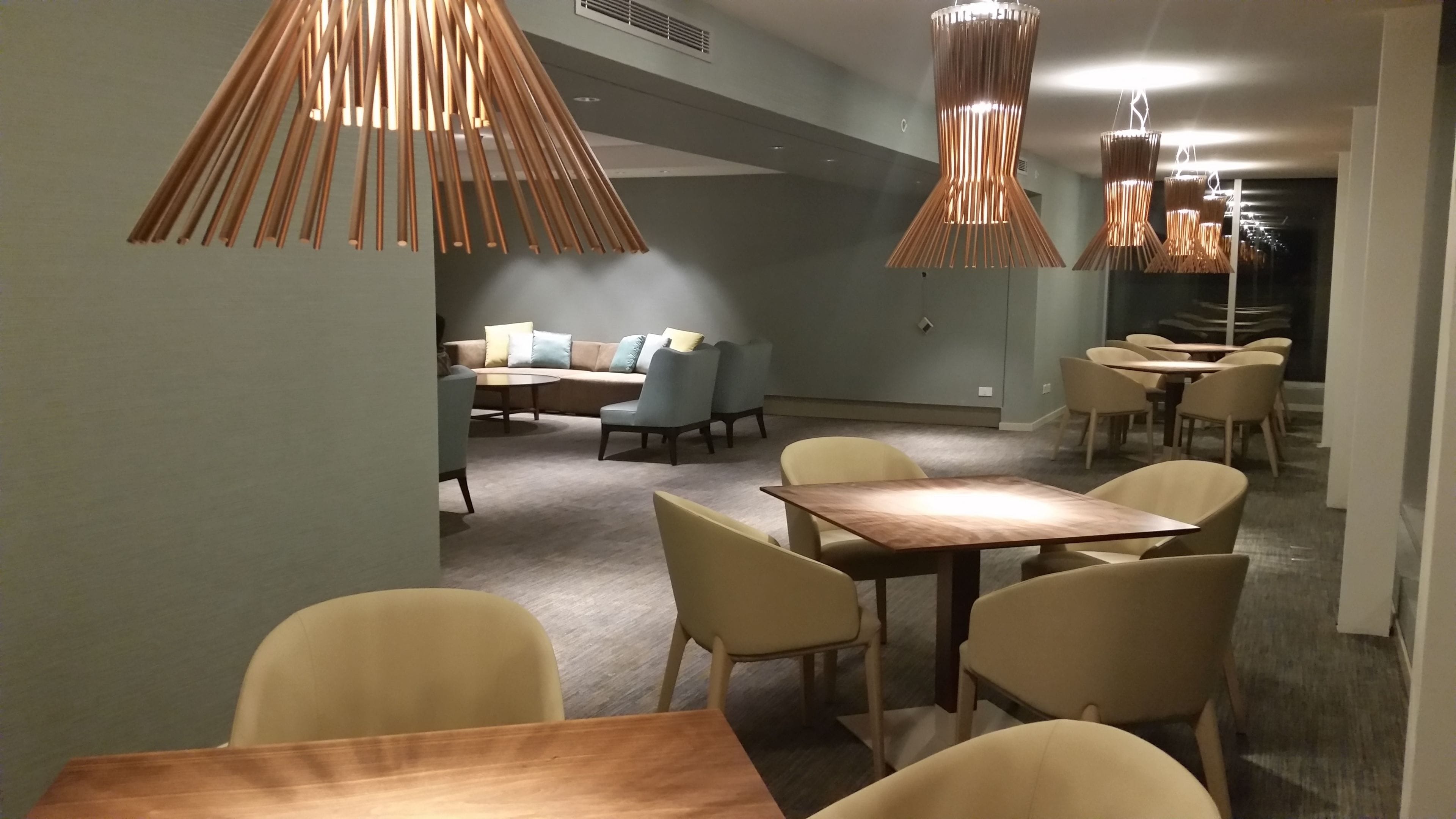 Un comedor moderno con mesas y sillas de madera, un conjunto de sofás e iluminación colgante.