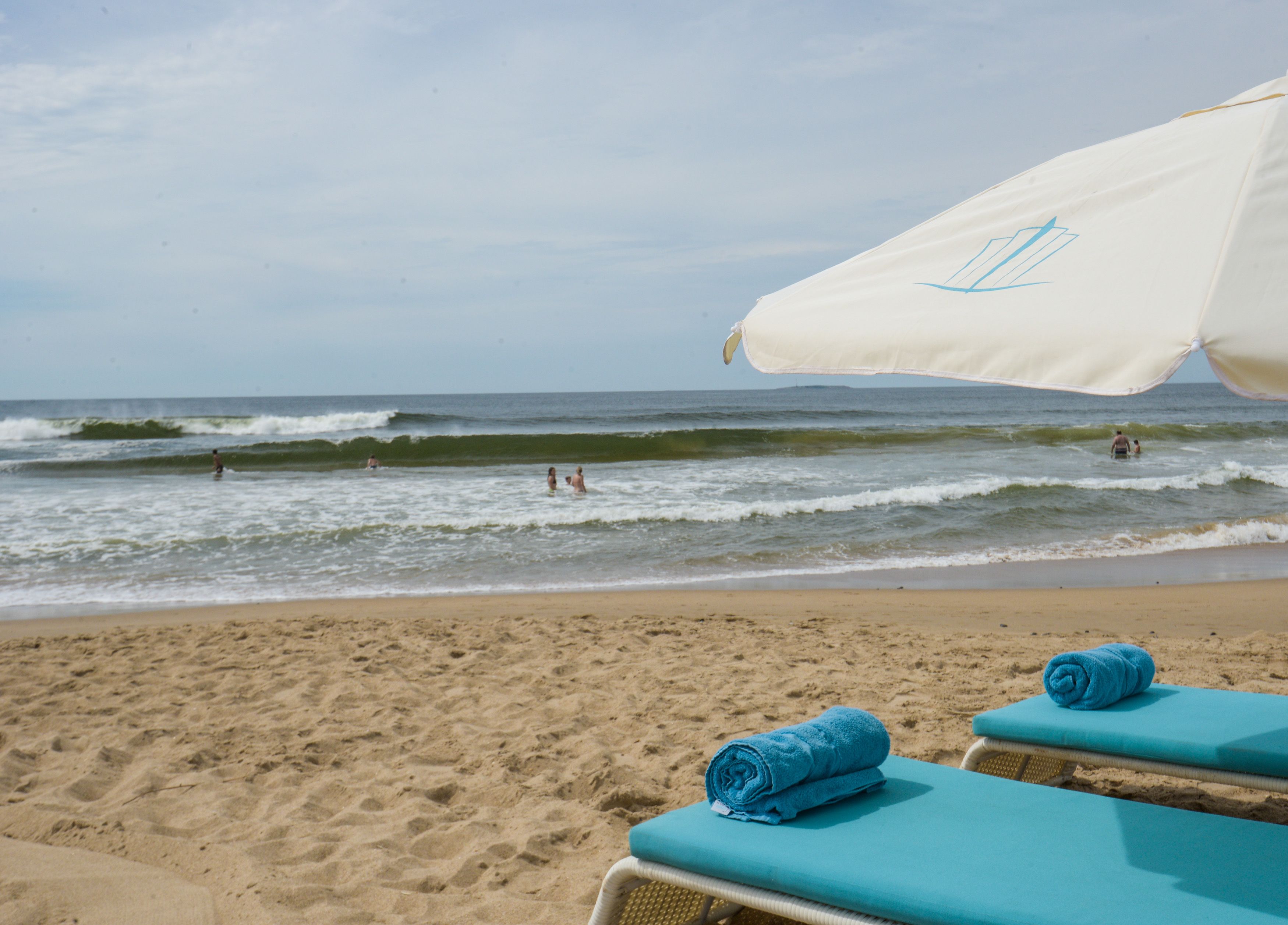 A beach with a white umbrella and two blue towels on lounge chairs.