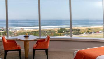 Habitación de hotel con un ventanal amplio que ofrece vistas a la playa y al océano.