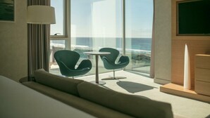 A modern hotel room with a large balcony, a sofa, two chairs, a small table, and a TV mounted on the wall. - The Grand Hotel Punta Del Este (Punta del Este)