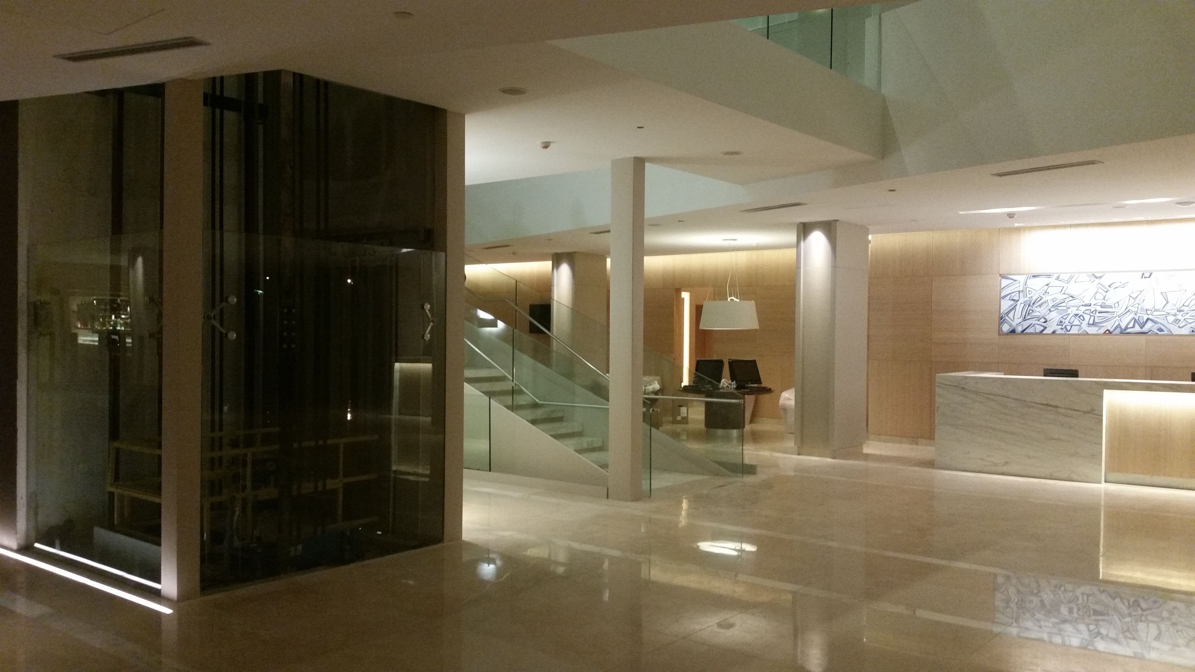 Een moderne lobby met een receptiebalie, een glazen lift en een trap.