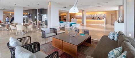 A modern hotel lobby with a reception desk, seating areas, and a staircase.