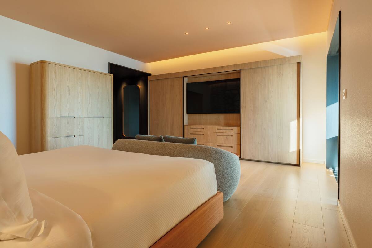 A modern bedroom with a large bed, built-in wardrobe, and a TV.