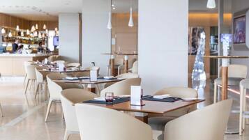 Un restaurante moderno con una zona de bar al fondo. Las mesas están dispuestas en línea, con sillas.