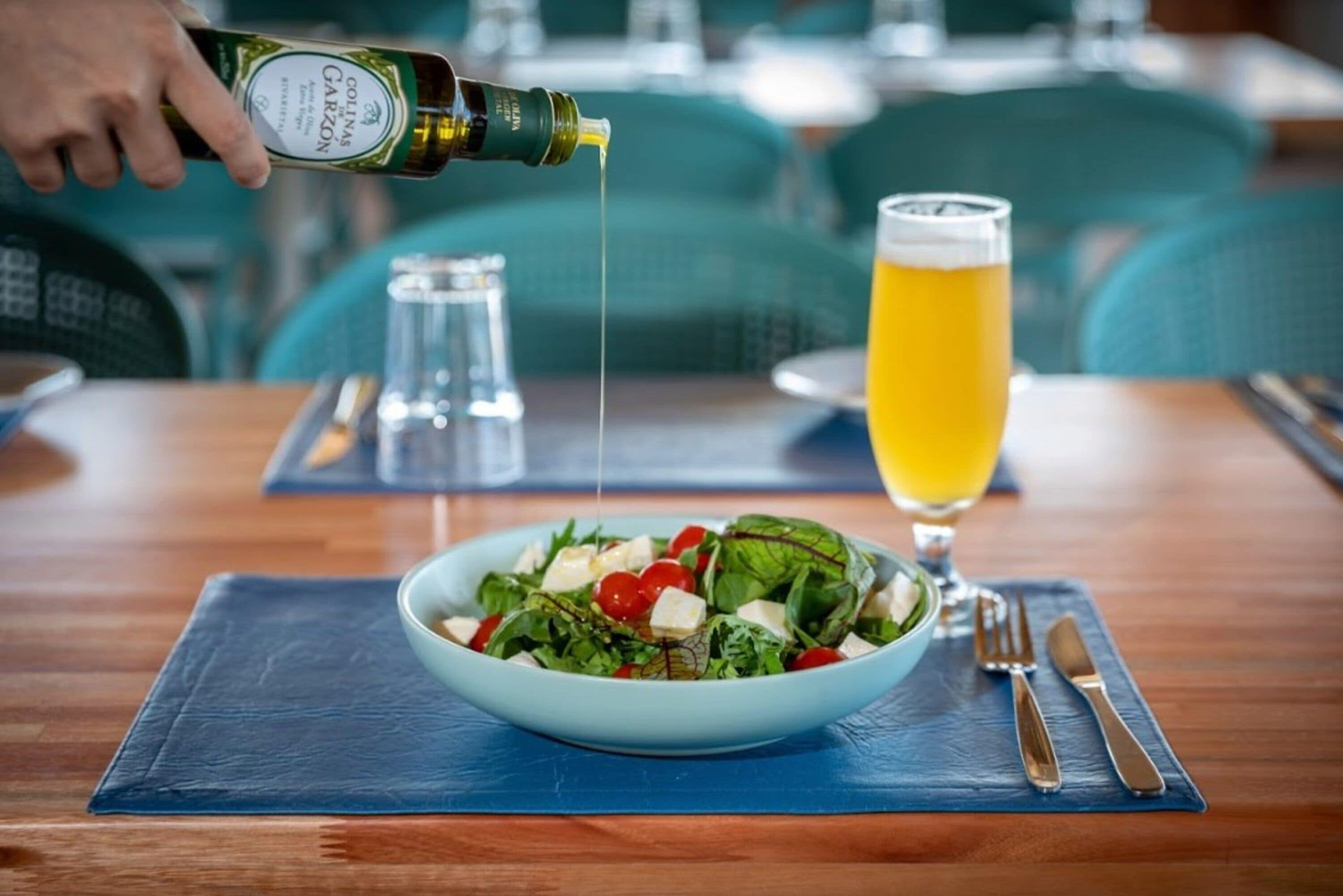 Un restaurante con una mesa donde se ve un ensaladero, una jarra de cerveza y una botella de vino siendo servida.