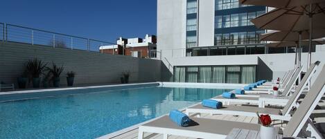 A poolside area with lounge chairs, umbrellas, and a clear blue pool.