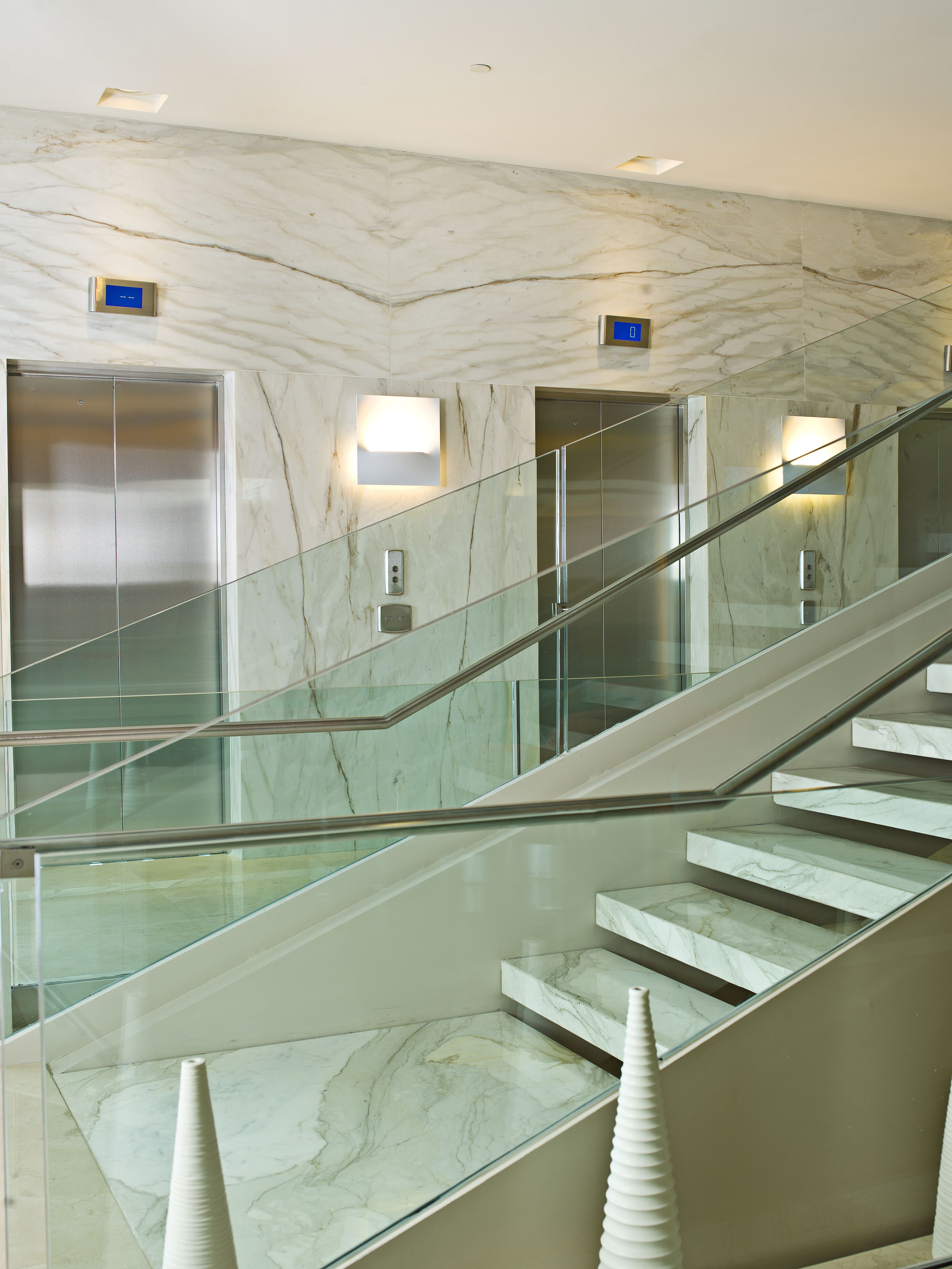 Un escalier en marbre avec des rampes en verre et un ascenseur moderne.