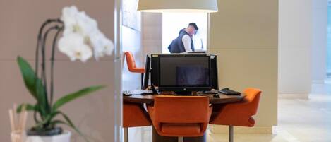 Un hall d’hôtel moderne avec un comptoir, deux fauteuils orange, une grande lampe et une plante en pot.