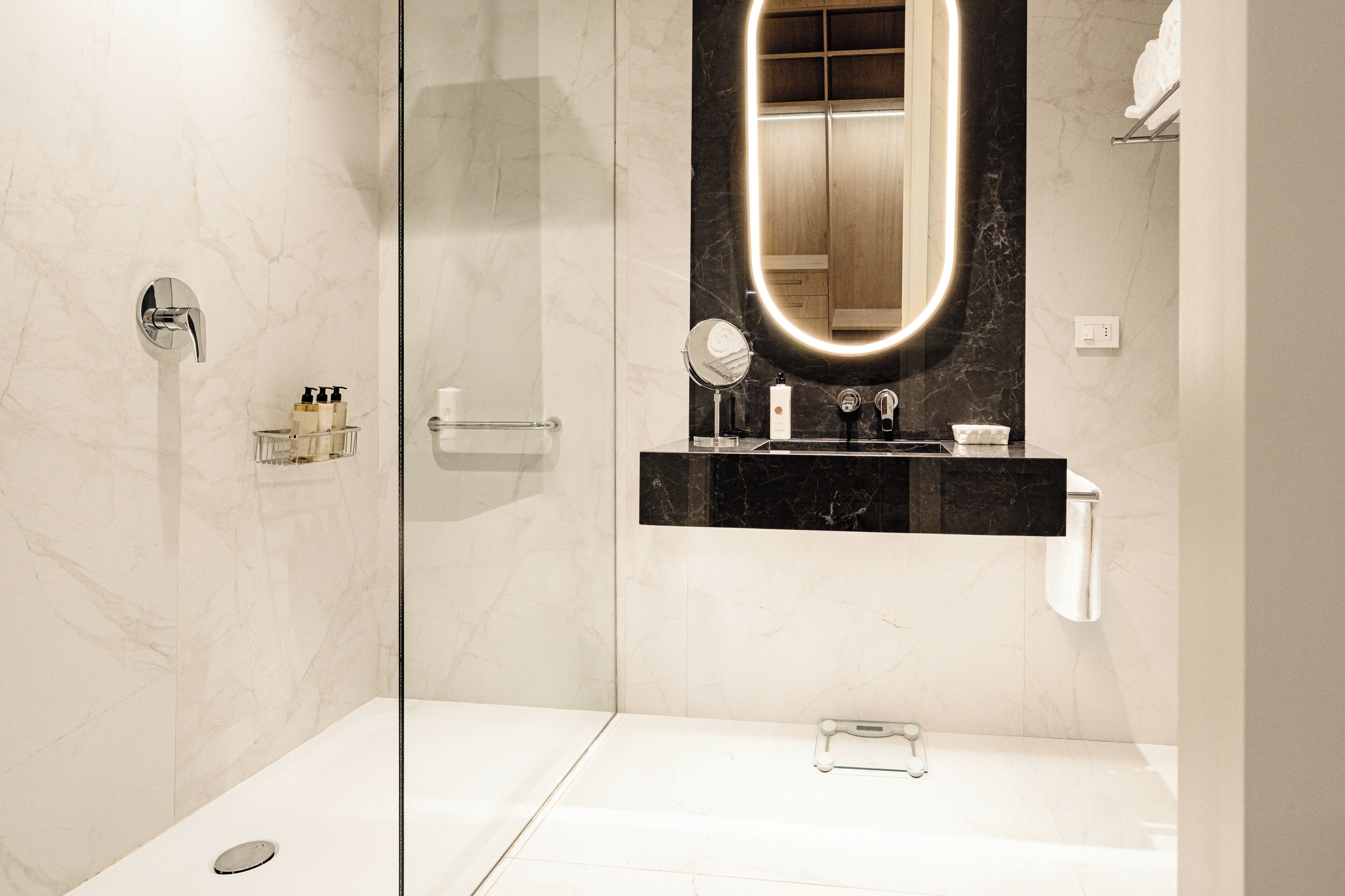 A modern bathroom with a glass-enclosed shower, a vanity with a black marble countertop, and a large mirror with a lighted frame.