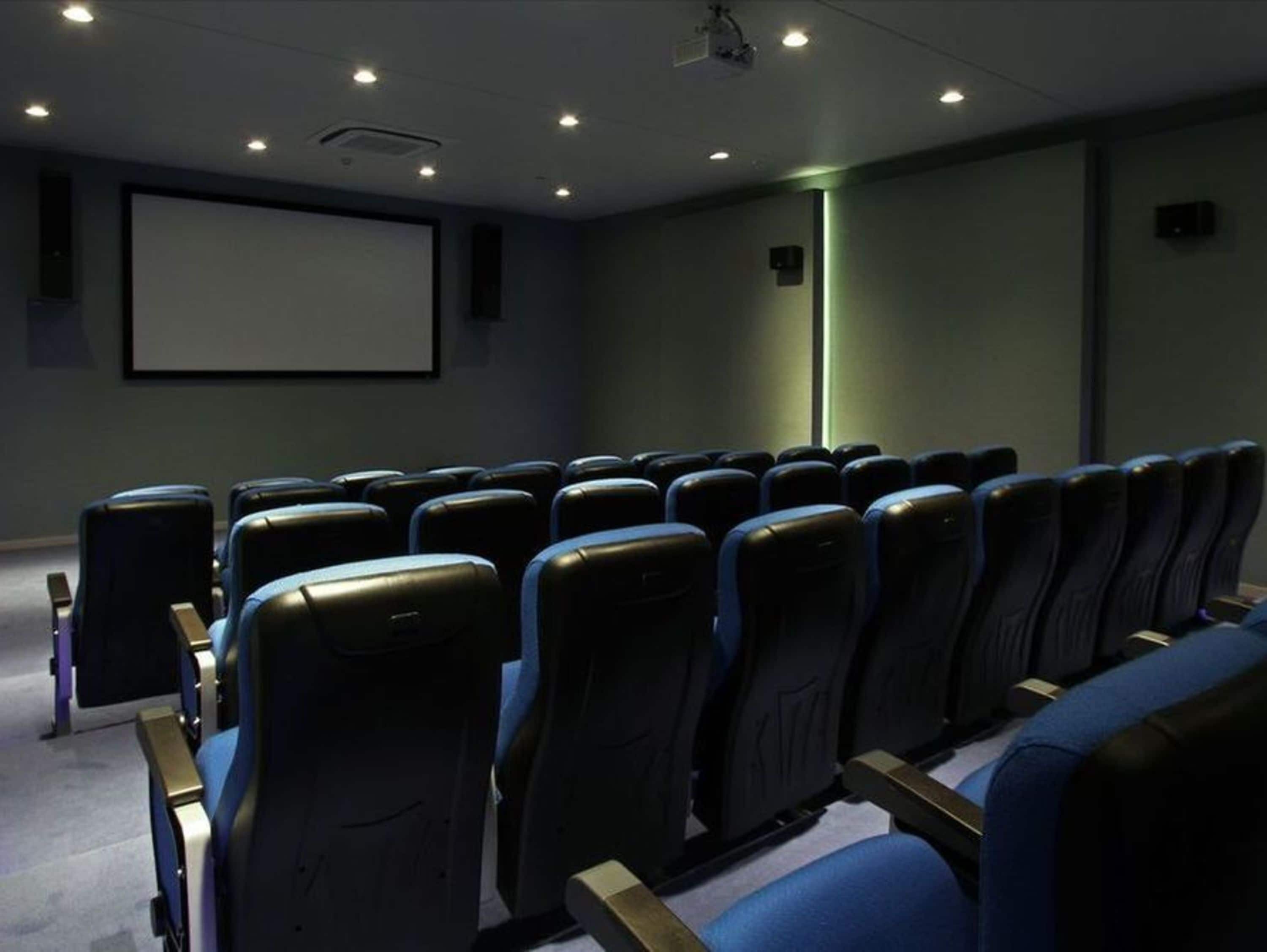 A movie theater with rows of seats, a large screen, and a projector.