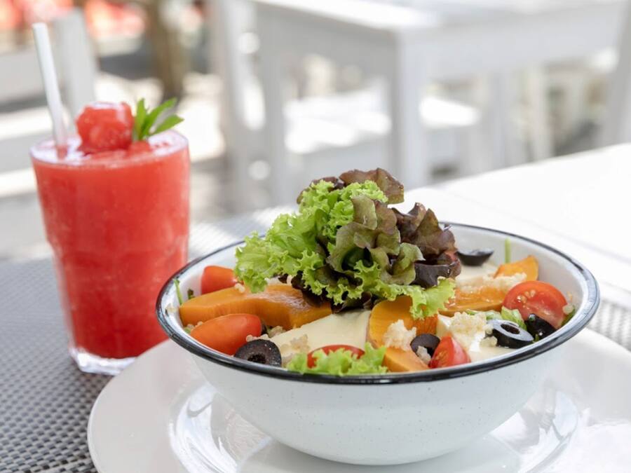 A bowl of salad with various vegetables and a red drink with a straw.