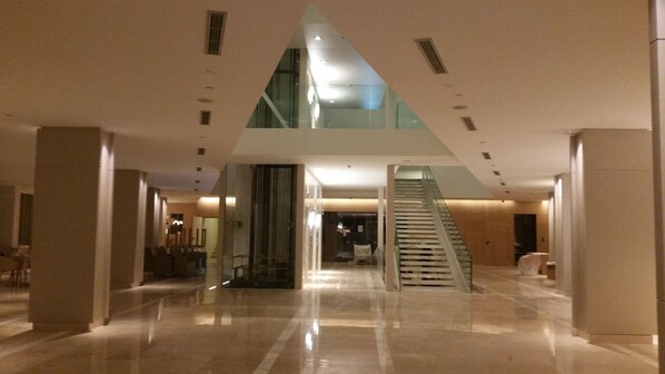 A spacious lobby with a high ceiling, a glass elevator, and a staircase. - The Grand Hotel Punta Del Este (Punta del Este)