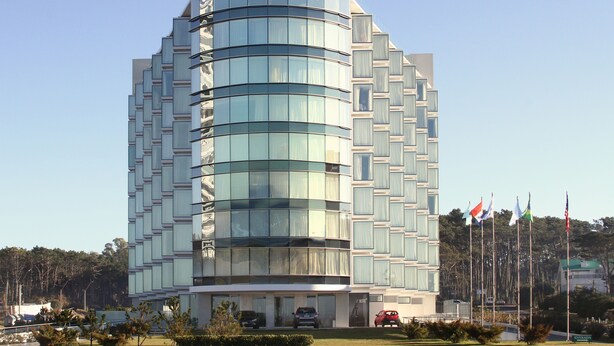 A modern building with a curved facade, multiple windows, and a flag display. - The Grand Hotel Punta Del Este (Punta del Este)