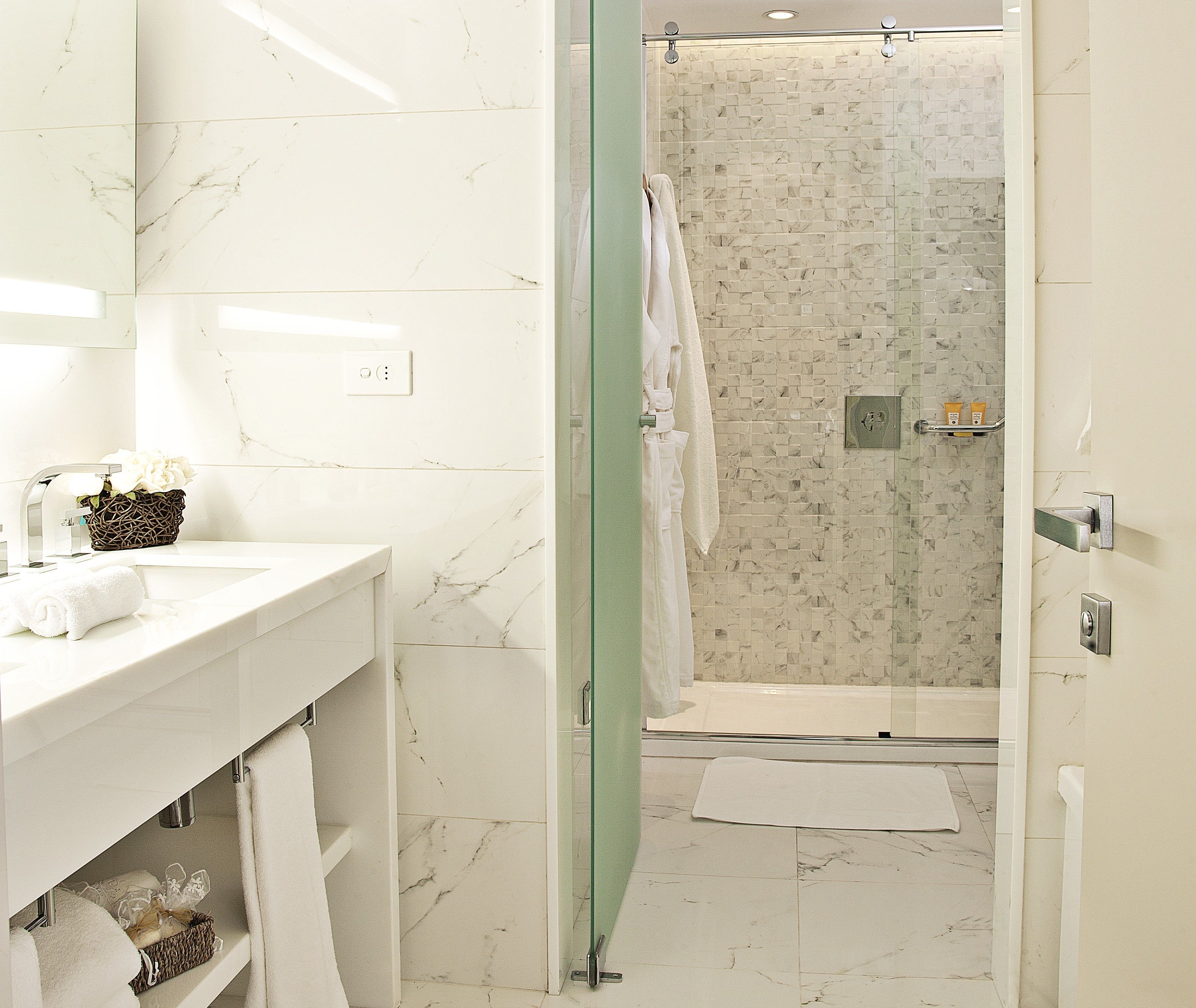 Un baño moderno con tocador de mármol, cabina de ducha de vidrio y una toalla blanca en el suelo.