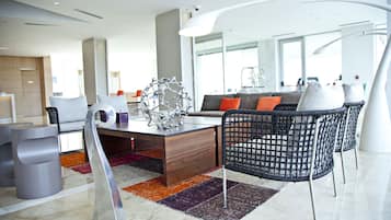 Um hall de hotel moderno com uma receção em madeira, assentos confortáveis e uma grande janela com vista para a cidade.