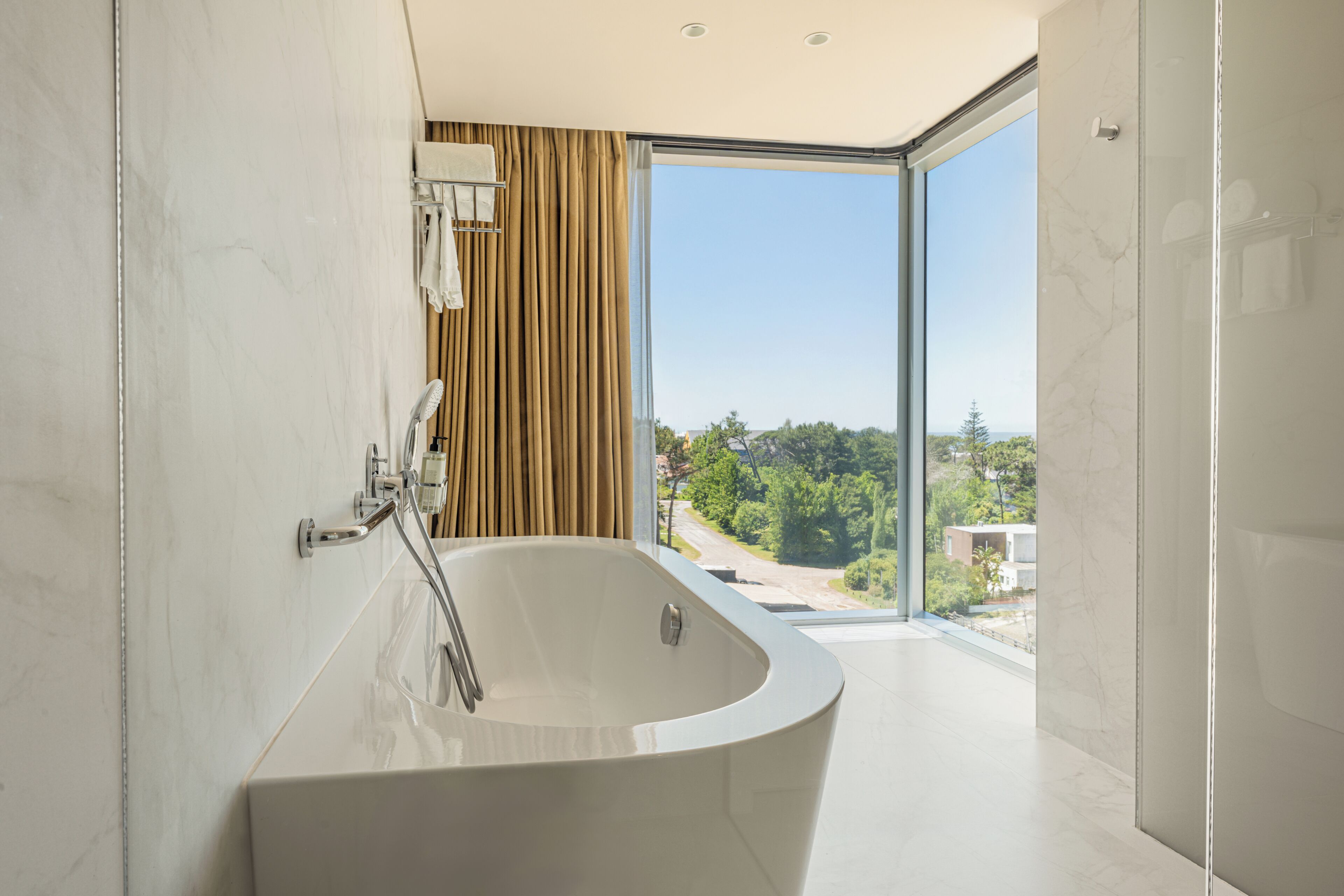 A modern bathroom with a freestanding bathtub, a glass shower enclosure, and a view of a residential area.