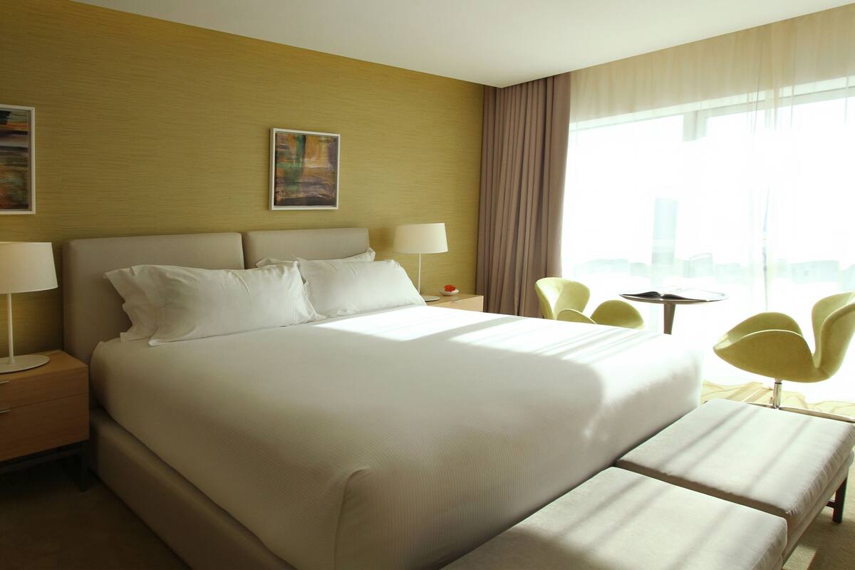 A hotel room with a large bed, two bedside tables, a desk, a chair, and a window with curtains.