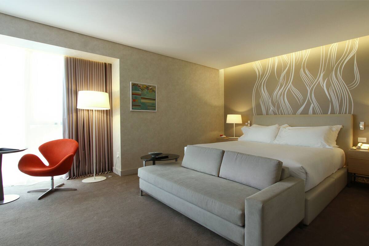 A hotel room with a large bed, a sofa, a desk, and a chair.