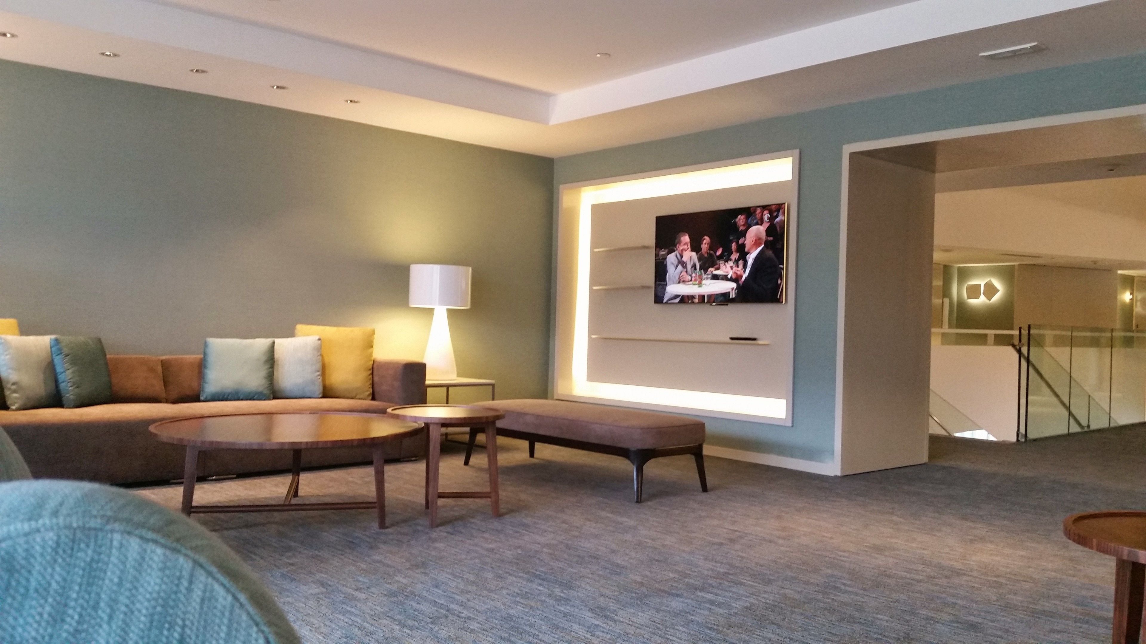 Ein modernes Wohnzimmer mit Sofa, Couchtisch und Hocker, einem an der Wand befestigten Flachbildfernseher und einer Treppe, die zu einer oberen Ebene führt.
