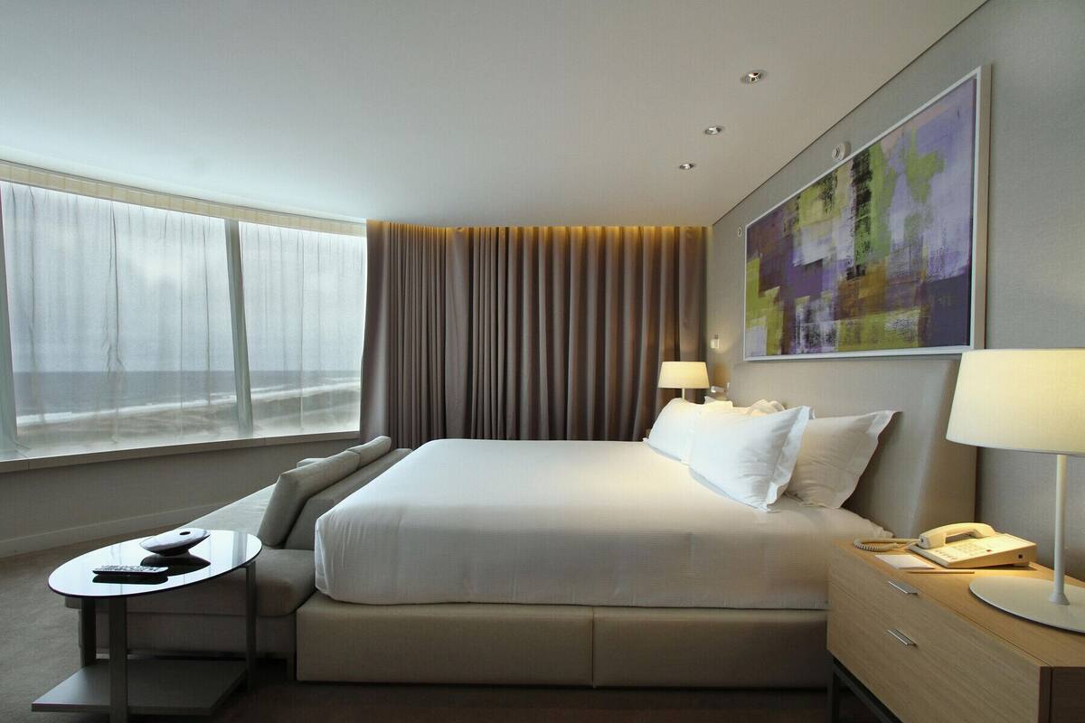 A hotel room with a bed, bedside table, lamp, and a painting on the wall.