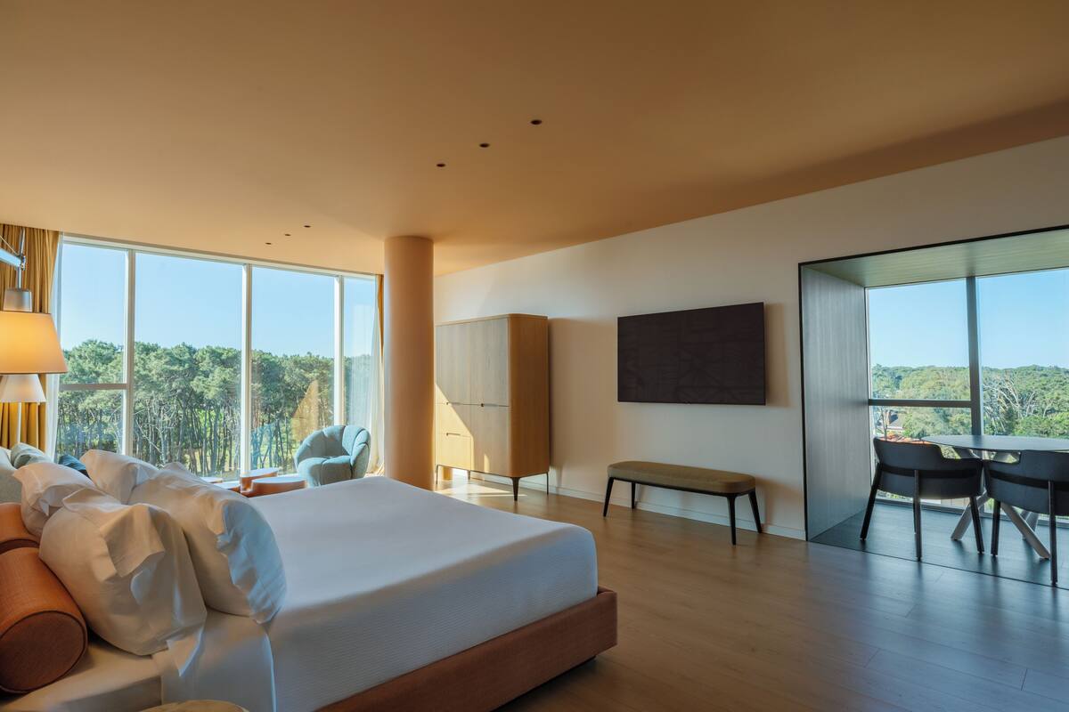 A modern hotel room with a large bed, a desk, and a view of the outdoors.
