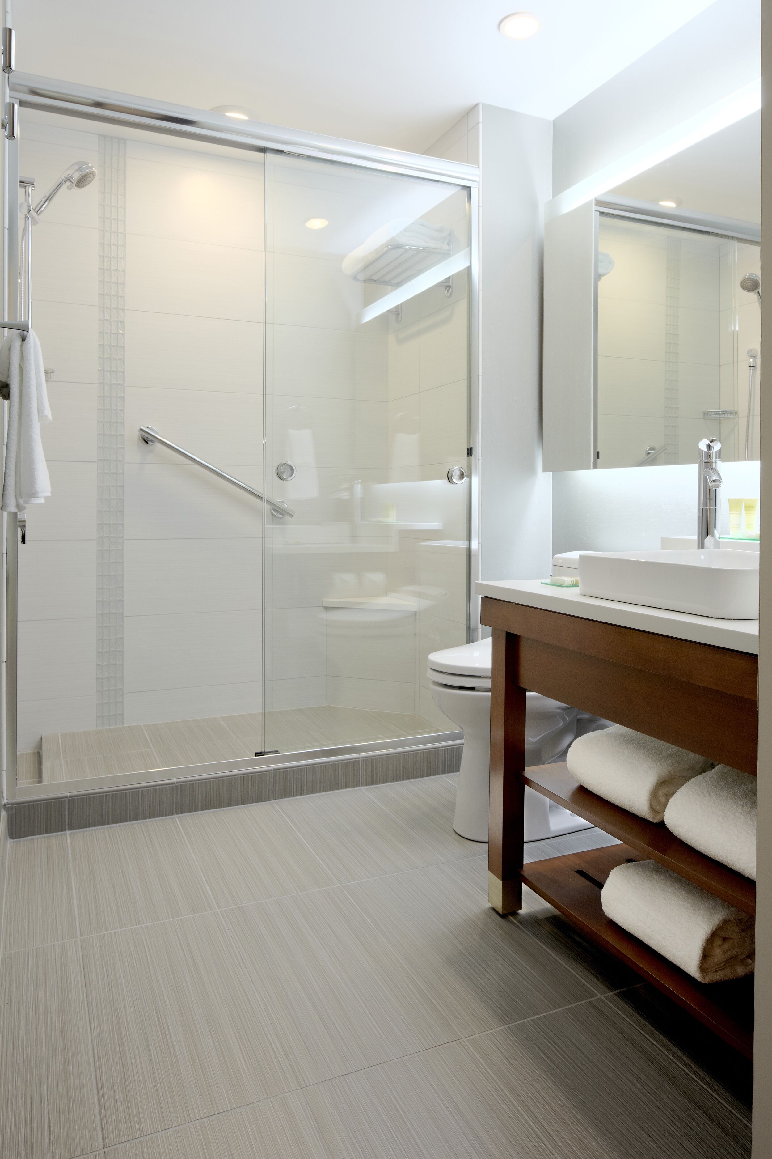 Une salle de bain moderne avec une douche à parois de verre, des toilettes blanches et un meuble-lavabo en bois avec un miroir.