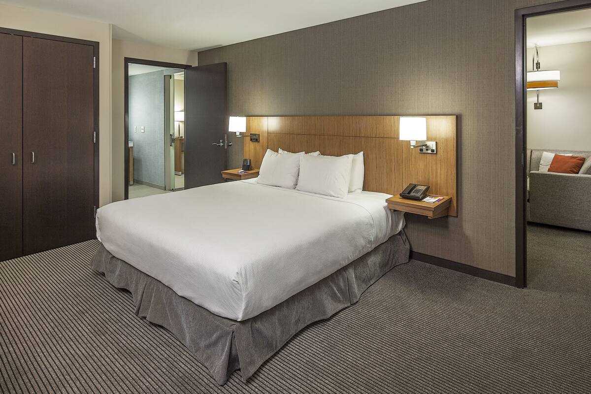 Une chambre d’hôtel avec un grand lit, une tête de lit en bois, des lampes de chevet, une table de chevet et une armoire.