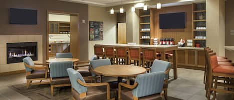 Un hall d’hôtel doté d’une cheminée, d’un bar et d’un espace salon avec des fauteuils et des tables.