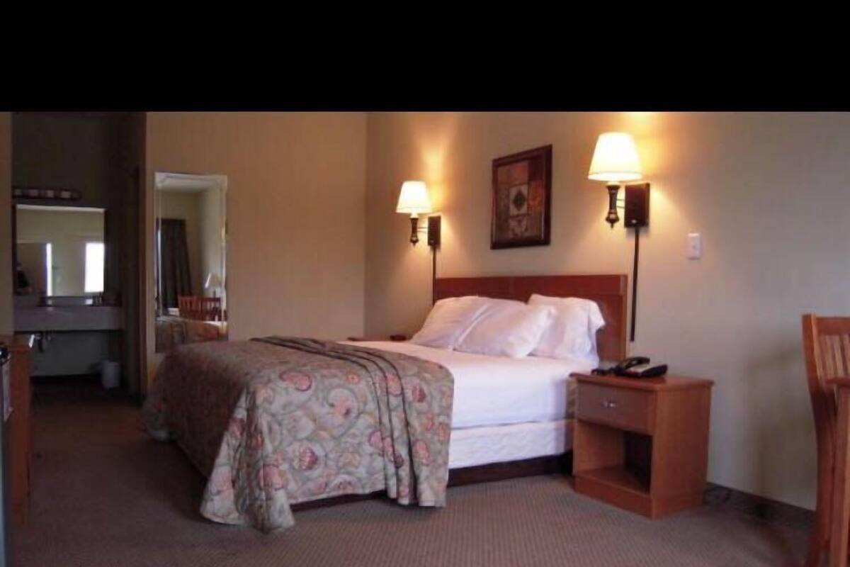 A hotel room with a bed, bedside tables, a nightstand, a mirror, and a door leading to another room.