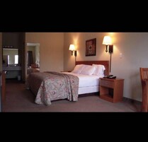 Una habitación de hotel con cama, mesitas de noche, un espejo y una puerta que da a otra estancia.