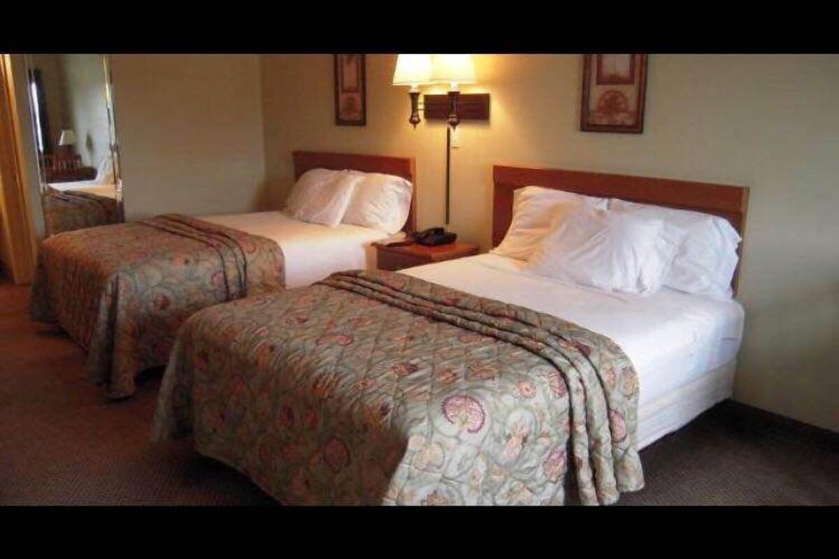 A hotel room with two beds, each with a patterned bedspread, a nightstand with a lamp, and a framed picture on the wall.