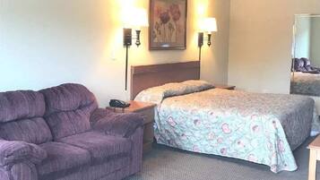 Quarto de hotel com cama, sofá, mesa de cabeceira, luminária e um quadro na parede.