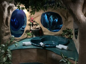 A spa area with a hot tub, two large oval windows, and surrounding greenery. - Designer Inn & Suites (Toledo)