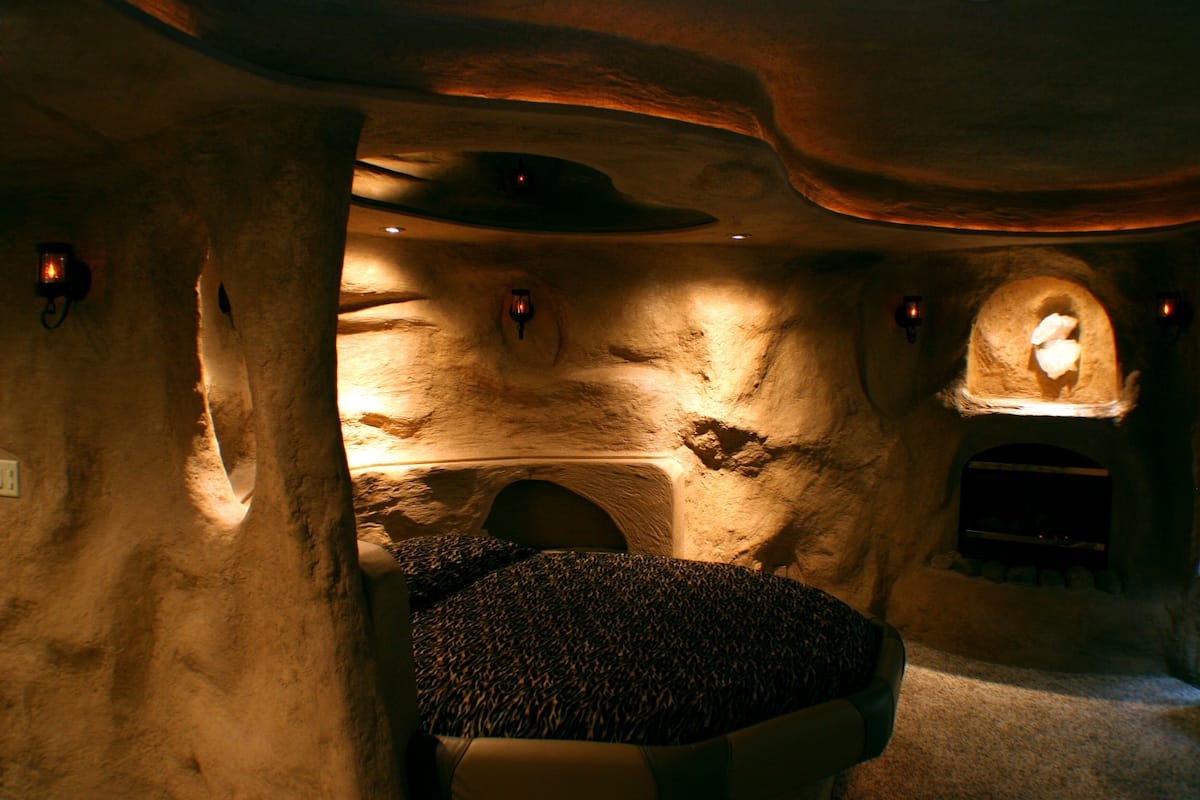 Um interior que lembra uma caverna, com área de estar central, paredes de pedra e iluminação embutida.