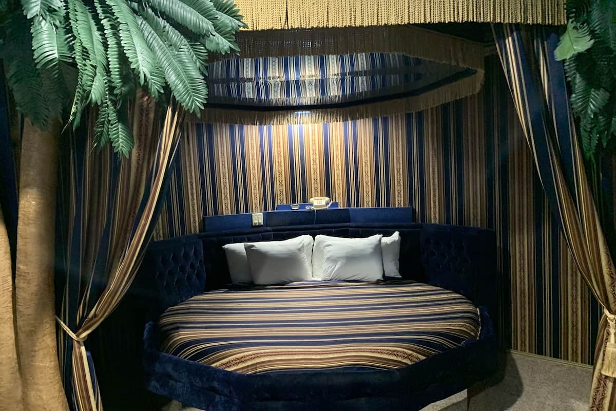 Quarto com cama estofada, roupa de cama listrada e cortina com padrão.