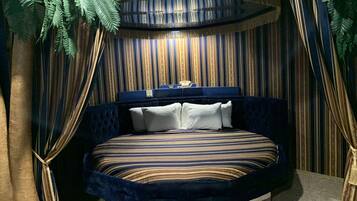 Un dormitorio con cama curvada, ropa de cama a rayas y un fondo de cortina estampado.