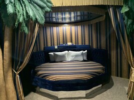 Un dormitorio con cama curvada, ropa de cama a rayas y un fondo de cortina estampado.