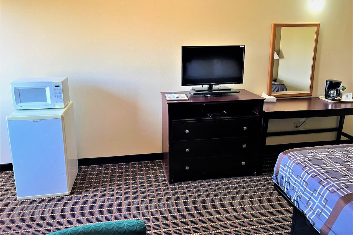 Quarto de hotel com cama, cômoda, televisão, micro-ondas e um pequeno refrigerador.