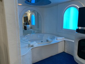 A modern bathroom with a large bathtub, a mirror, and a blue-lit window.