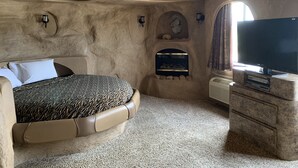 A bedroom with a unique stone wall design, a bed with a patterned cover, a fish tank, a flat-screen TV, and a built-in entertainment unit. - Designer Inn & Suites (Toledo)