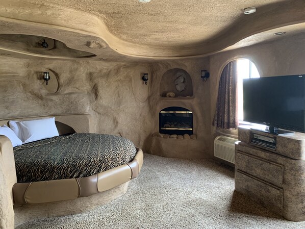 A bedroom with a unique stone wall design, a bed with a patterned cover, a fish tank, a flat-screen TV, and a built-in entertainment unit.