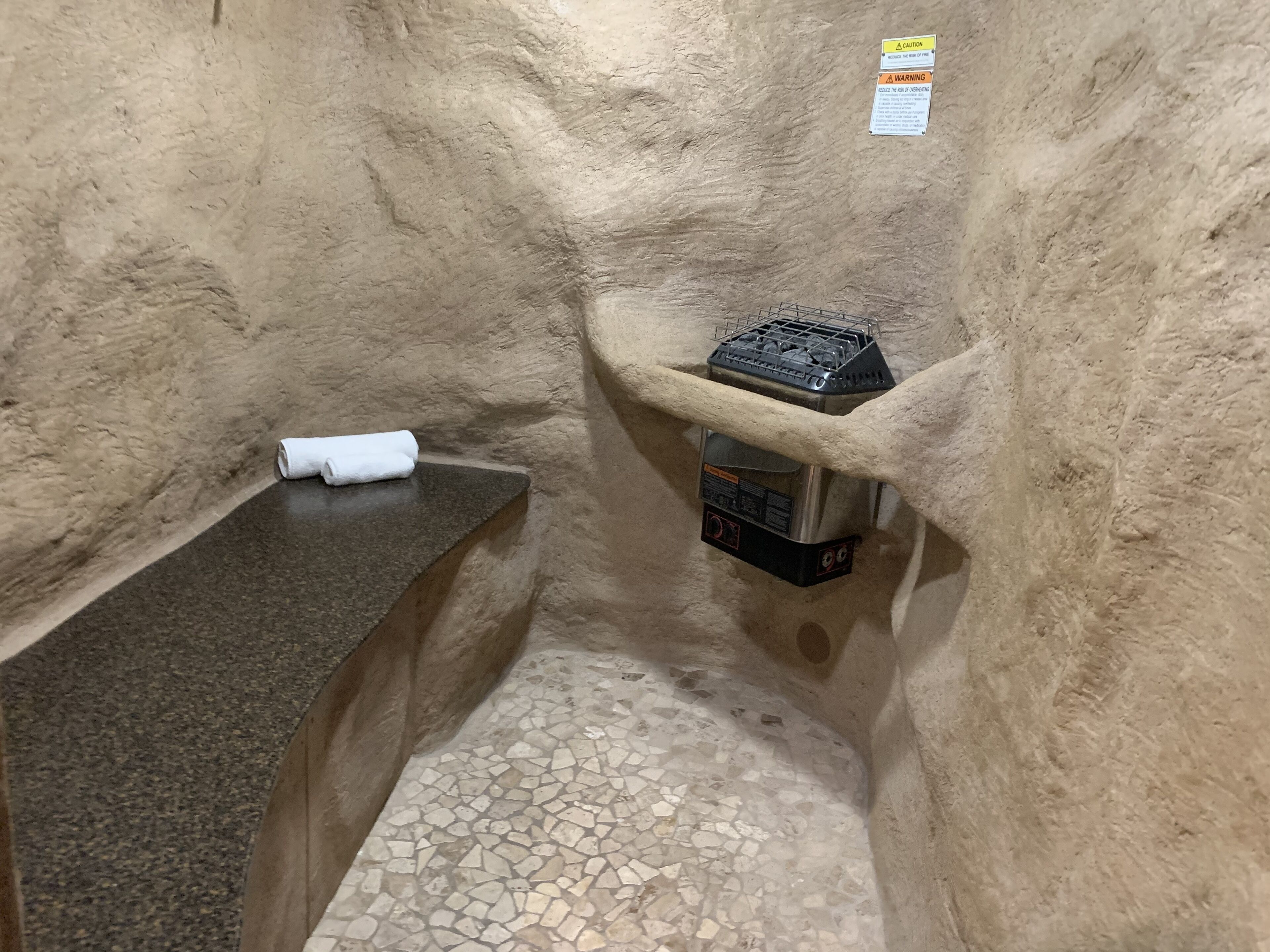 A small, enclosed bathroom with a tiled floor, a towel on a counter, and a portable heater.