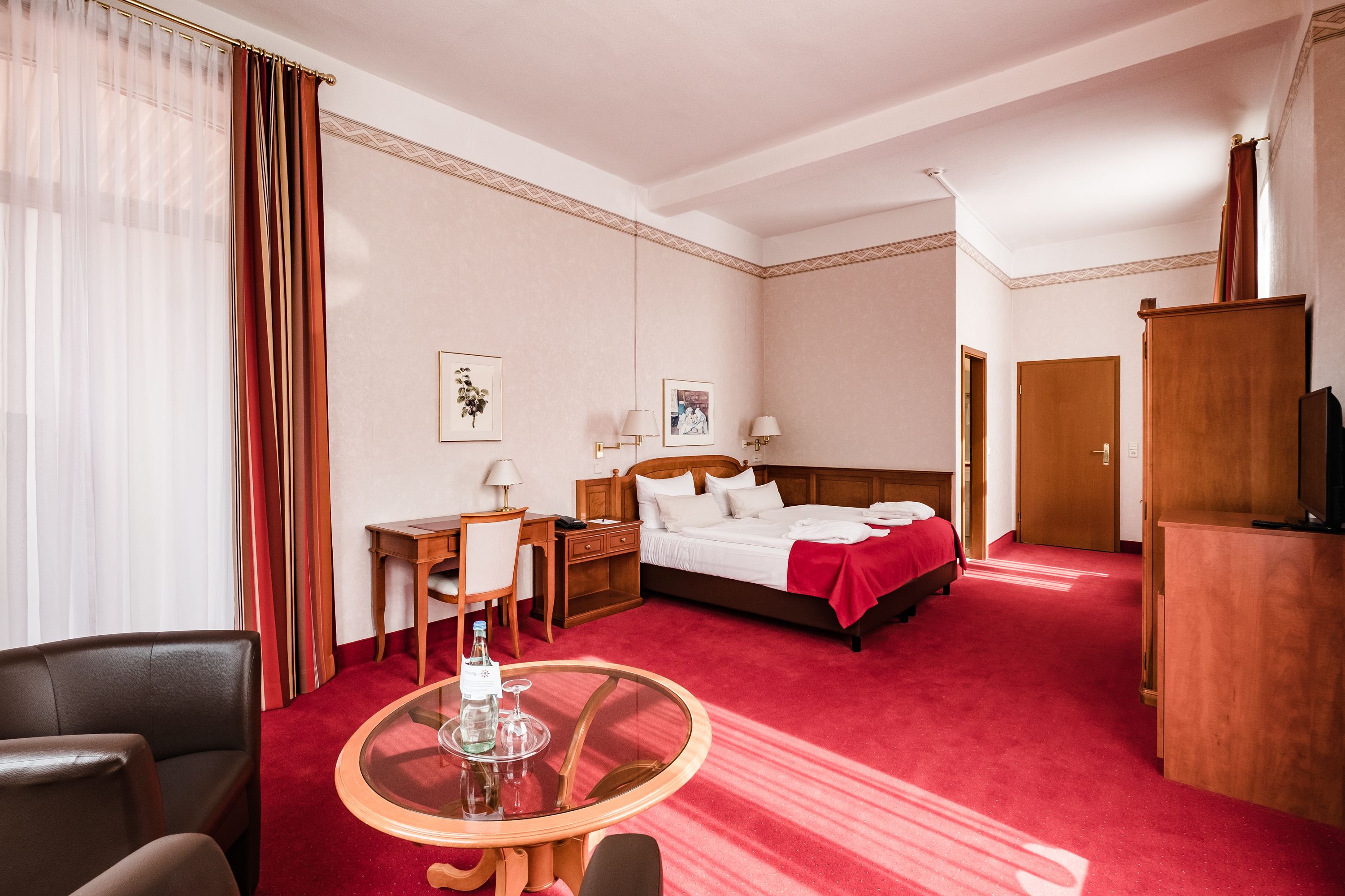 Una habitación de hotel con cama, mesita de noche, lámpara, silla y una pequeña mesa redonda con un vaso.