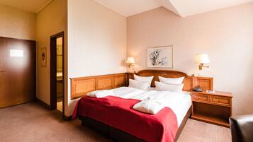 A hotel room with a large bed, two bedside tables with lamps, a wooden headboard, and a red bedspread.