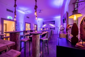 Un restaurante con mesas y sillas de madera, lámparas colgantes y una barra con botellas y un reloj.