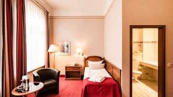 A hotel room with a bed, a chair, a nightstand, a lamp, and a view of the bathroom.